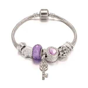 Close-up van de zilveren bedelarmband met paarse kristallen kralen en een sprankelende sleutel.