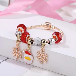 Primo piano del bracciale con charm natalizio in oro rosa con perline di vetro rosse e pendenti.