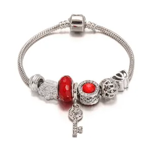 Zilveren charm armband met rode kralen en stralende sleutelhanger, elegante slangenketting.