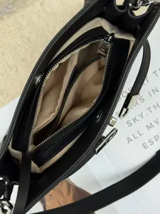 Primer plano del interior del bolso negro, mostrando compartimentos con cremallera y forro.