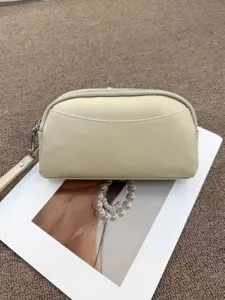 Minimalist leather clutch detail showing beige texture, metal zipper and wrist strap.