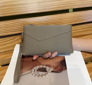 Close detail of the grey leather clutch bag showing fine grain texture, zipper and wrist strap.