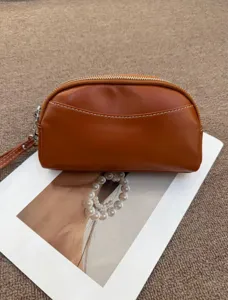 Brown leather dome clutch pouch detail shot with contrast stitching and metal zipper pull.