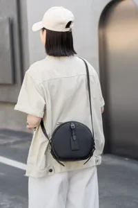 Detail view of the black round leather crossbody bag worn by a model in a street scene.