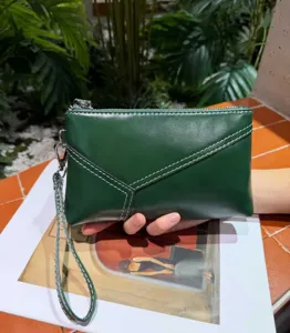 Detailed shot of dark green leather wristlet clutch bag, showcasing fine texture and wrist strap.
