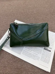 Detailed view of dark green leather clutch bag with contrast white stitching and wrist strap.
