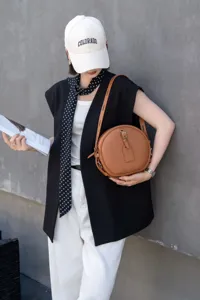 Detailed close-up of a brown leather round crossbody bag worn by a model in a stylish look.