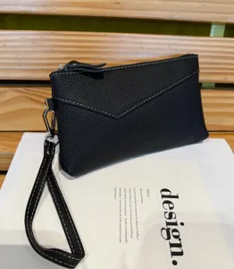 Black genuine leather women's clutch bag with zipper and wrist strap, detailed view.