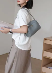 Detail shot of grey leather shoulder bag worn by model, showing natural texture and hardware.