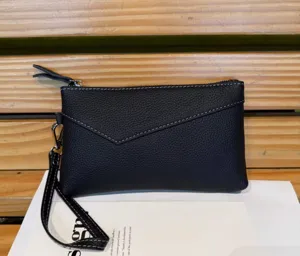 Close up detail view of black leather clutch bag featuring contrast white stitching and wristlet.