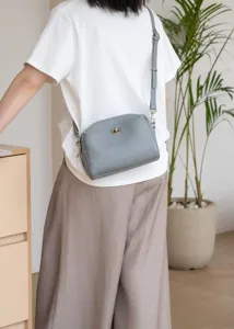 Grey leather crossbody shoulder bag detail showcasing natural pebble grain texture and metal lock.