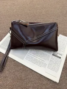 Detailed close-up of brown genuine leather clutch bag with white stitching and wrist strap.