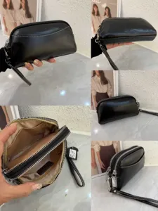 Detail view of black leather women's clutch bag with multiple zippers and wrist strap.