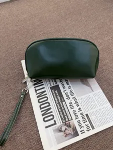 Dark green leather clutch detail view, showing smooth curved shape and metallic zipper.