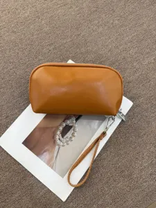 Portable brown leather cosmetic bag, semi-circular clutch handbag for travel and daily use.