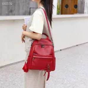 Detailed shot of a stylish red genuine leather backpack worn by a model in outdoor setting.