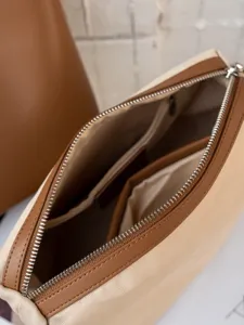 Élégant sac à bandoulière en toile beige et marron avec fermeture éclair et intérieur spacieux.