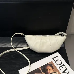 Closeup detail of minimalist leather crescent crossbody bag in off-white with fine strap.
