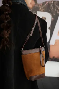 Dettaglio borsa a secchiello bicolore in camoscio marrone, tracolla elegante per uso quotidiano.