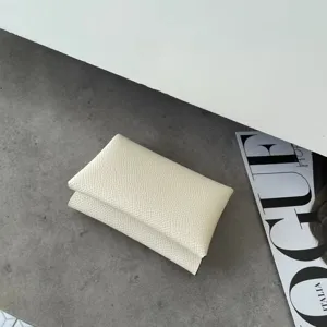 Detailed view of minimalist cream white leather card holder with fine texture on grey tabletop.