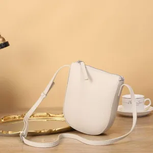 Sac bandoulière vertical en cuir beige pour téléphone avec fermeture éclair et sangle.