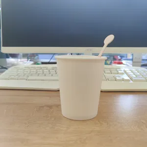 Detailed shot of a disposable paper cup with a wooden coffee stirrer placed on wooden desk.