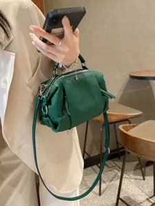 Dark green top cowhide leather handbag detail, showing texture, dual zippers and strap.
