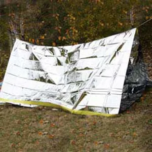 Silver reflective emergency thermal blanket set up as outdoor survival shelter for camping.