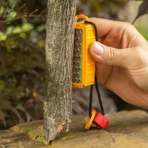 Outdoor survival flint fire starter detail showing metal scraper usage against tree bark.