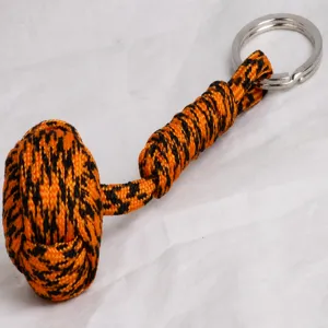 Paracord monkey fist keychain detail, orange and black woven outdoor survival rope ring accessory.