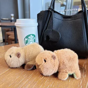 Cute capybara plush keychain detail shot, soft plush toy pendant lifestyle display on wooden desk.