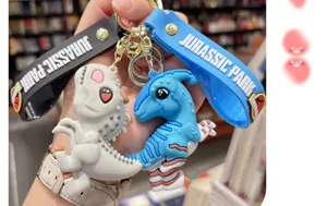 Vue détaillée du joli porte-clés dinosaure cartoon, matière PVC souple avec anneaux.
