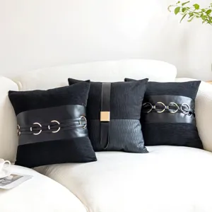 Detail of black decorative throw pillow with leather strap and metal ring accent on sofa.