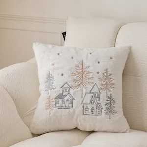 White plush Christmas throw pillow cover with winter house and tree embroidery detail.