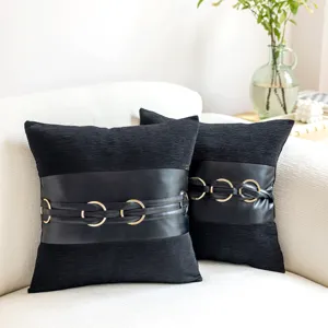 Close-up detail of black decorative throw pillow with faux leather belt and gold rings.