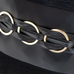 Black faux leather throw pillow cover detail with gold metal rings and braided straps.