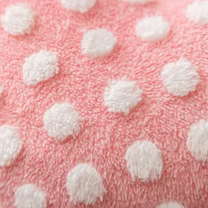 Close up of pink plush pillow cover with white fluffy dots, soft and cozy texture detail.