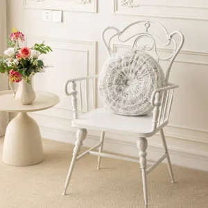 Detailed view of a round textured plush throw pillow displayed on a vintage white accent chair.