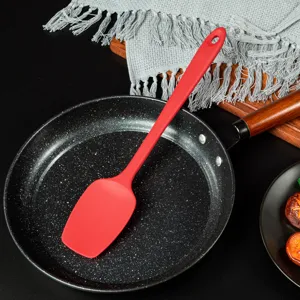 Vue détaillée d'une spatule de cuisson en silicone rouge dans une poêle de cuisine.