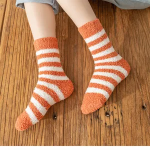 Close-up detail of cozy orange and white striped coral fleece fuzzy socks for women home wear.