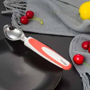 Stainless steel ice cream scoop detail view, ergonomic handle on black plate with fruit.