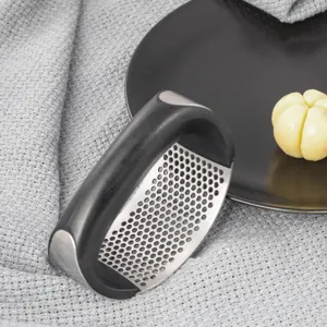 Stainless steel rocker garlic press detail view, ergonomic black handle kitchen tool close-up.