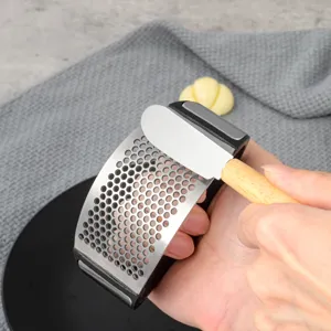 Stainless steel garlic press detail showing ergonomic wooden handle and perforated curved mesh surface.