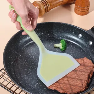 Close-up of a green silicone spatula cooking steak in a frying pan for kitchen use.