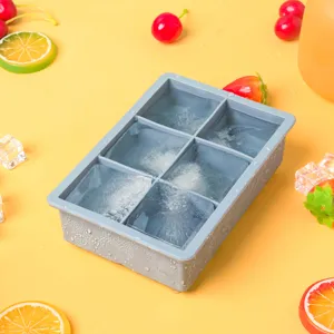 Détail de moule à glaçons en silicone gris avec 6 compartiments et glaçons sur fond de fruits jaunes.