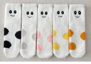 Nahaufnahme flauschiger Korallenfleece-Socken mit süßen bestickten Gesichtern und bunten Punkten.