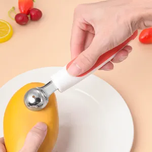 Detail view of the stainless steel fruit melon baller in use, scooping mango easily.