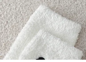 Nahaufnahme des weichen weißen Korallenfleece-Stoffs mit feiner schwarzer Stickerei.