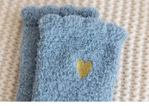 Close-up detail of cozy fluffy blue winter warm socks featuring a cute gold embroidered heart.