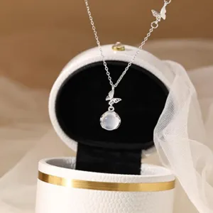 Close-up detail shot of a silver butterfly necklace with white gemstone pendant inside a box.